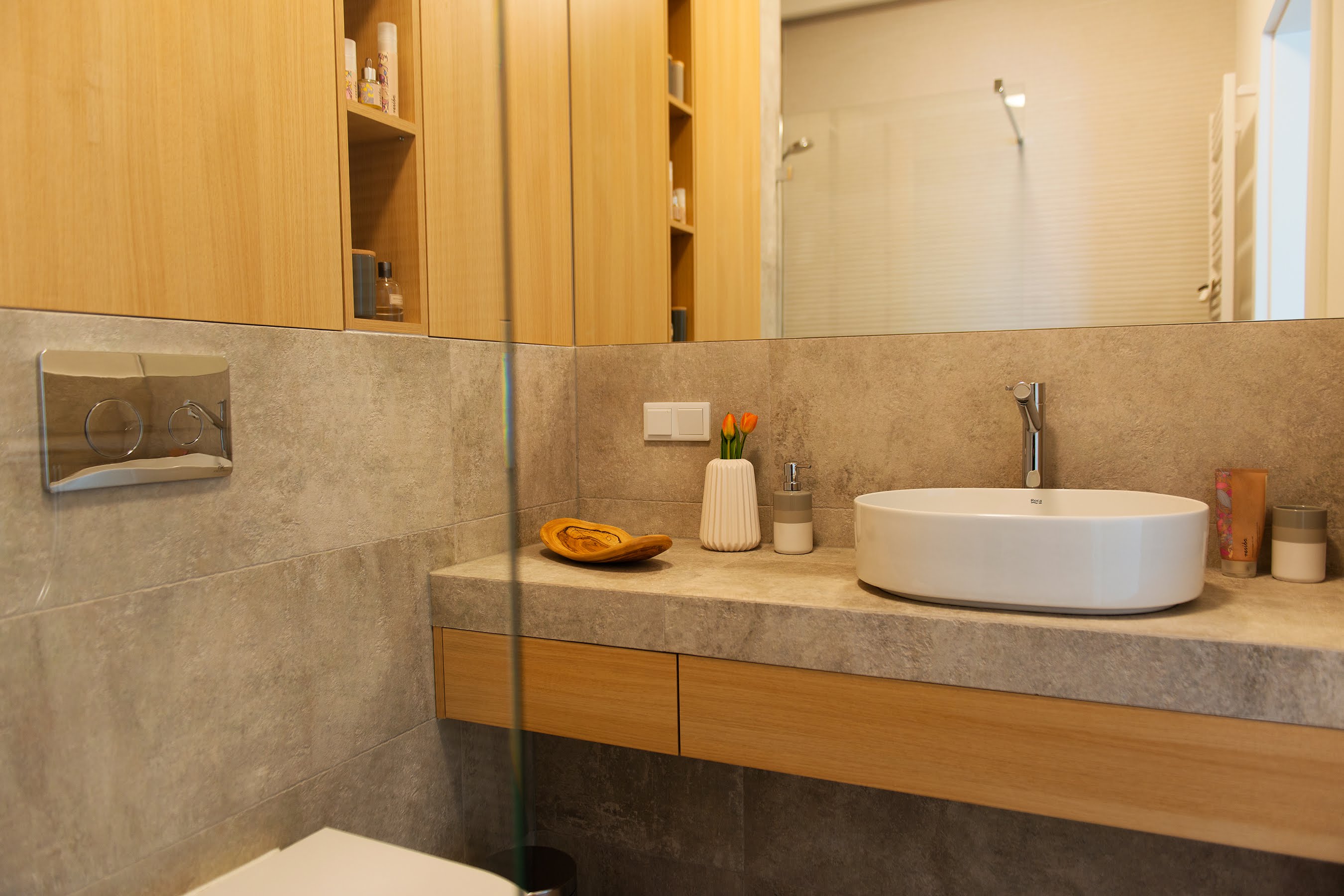 Duże lustro optycznie powiększa łazienkę i odbija oświetloną dekoracyjnie ścianę pod prysznicem.